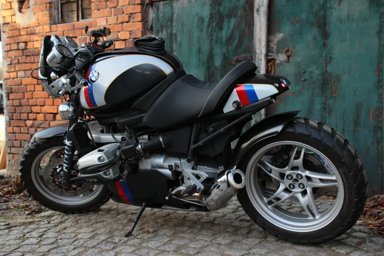 Stylowy motocykl BMW R 1100 R z charakterystycznymi pasami w barwach narodowych, zaparkowany na bruku.