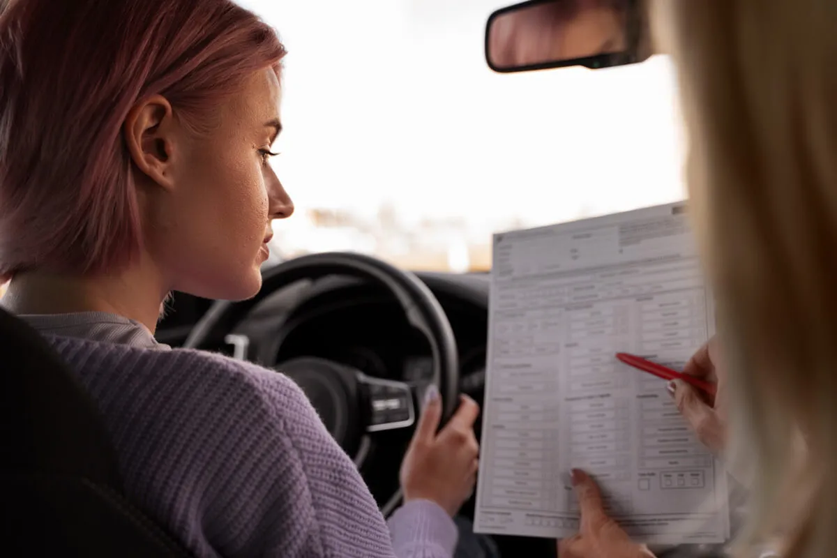 Młoda kobieta z r&oacute;żowymi włosami w samochodzie uczy się, ile kosztuje prawo jazdy, analizując dokument z instruktorem.