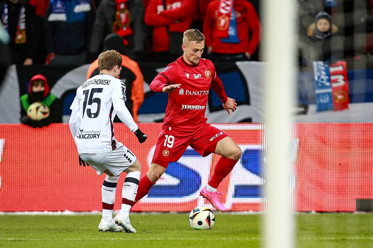 Piłkarze walczą o piłkę na boisku. Kibice na trybunach śledzą emocje, zastanawiając się, ile zostalo kolejek w ekstraklasie.