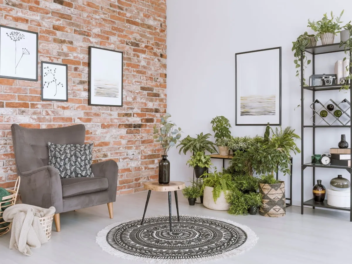 Przytulny salon z ceglaną ścianą, wygodnym fotelem i mn&oacute;stwem roślin. Inspiracja, jak zrobic cegle w aranżacji wnętrz.