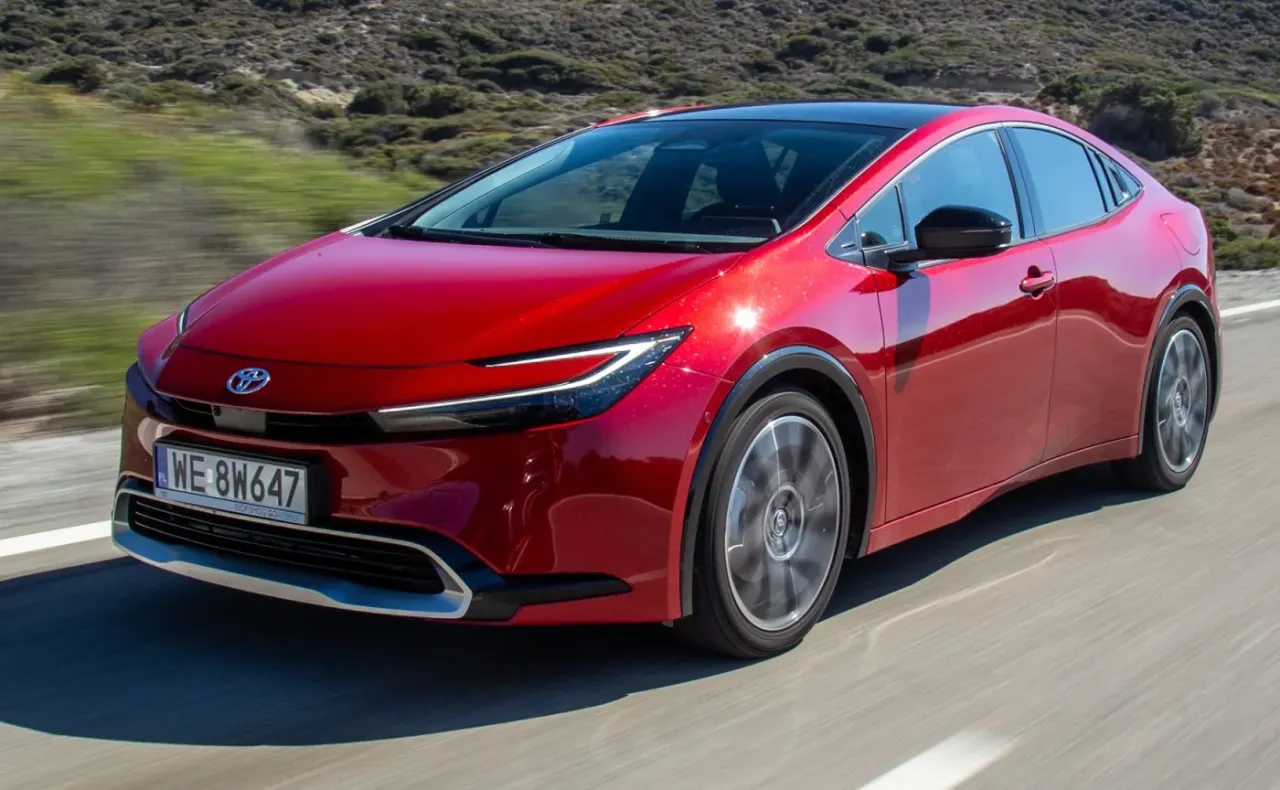 Czerwona Toyota Prius jedzie po drodze. Zastanawiasz się, ile pali Toyota Prius? Ten model jest bardzo oszczędny.