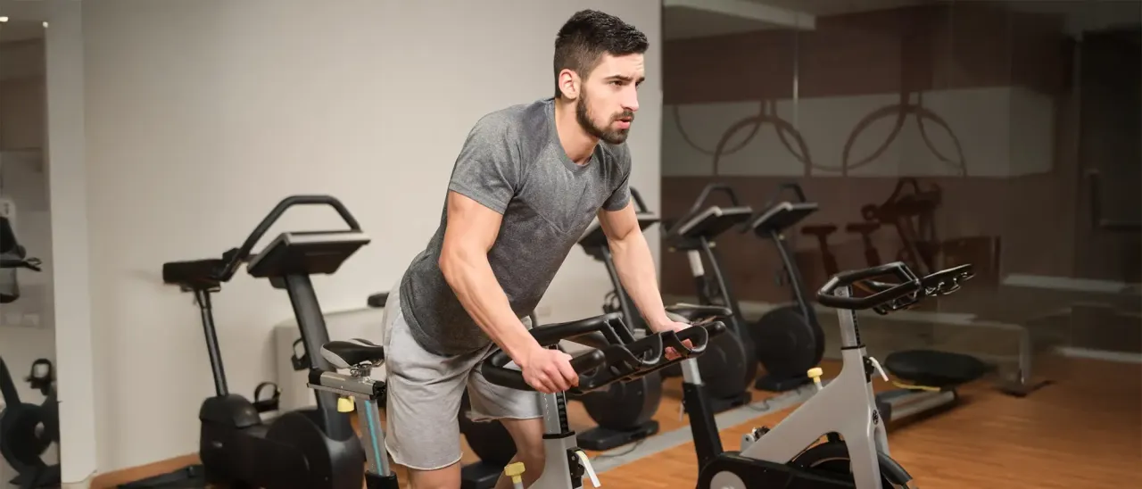 Mężczyzna ćwiczy na rowerze stacjonarnym, zastanawiając się, czy robić cardio na masie.