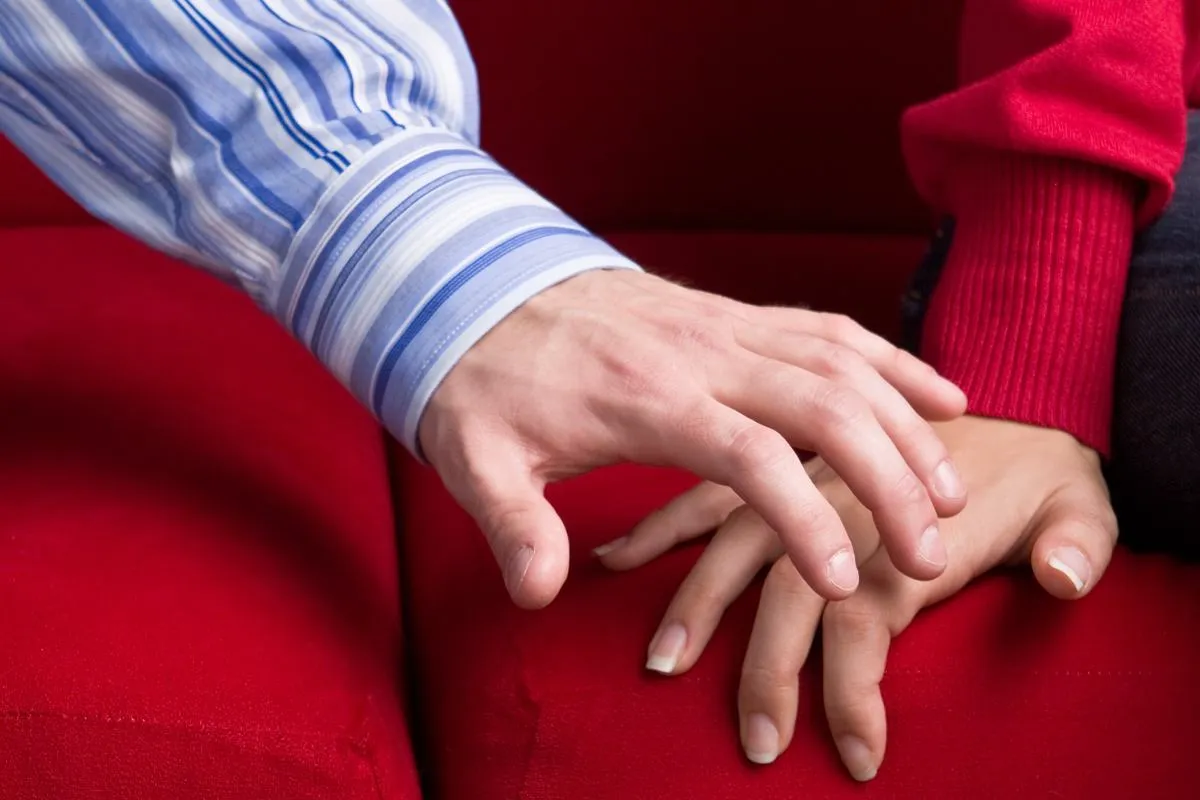 Delikatny dotyk dłoni na czerwonej kanapie. To obraz związku z wrażliwym facetem, kt&oacute;ry okazuje czułość.