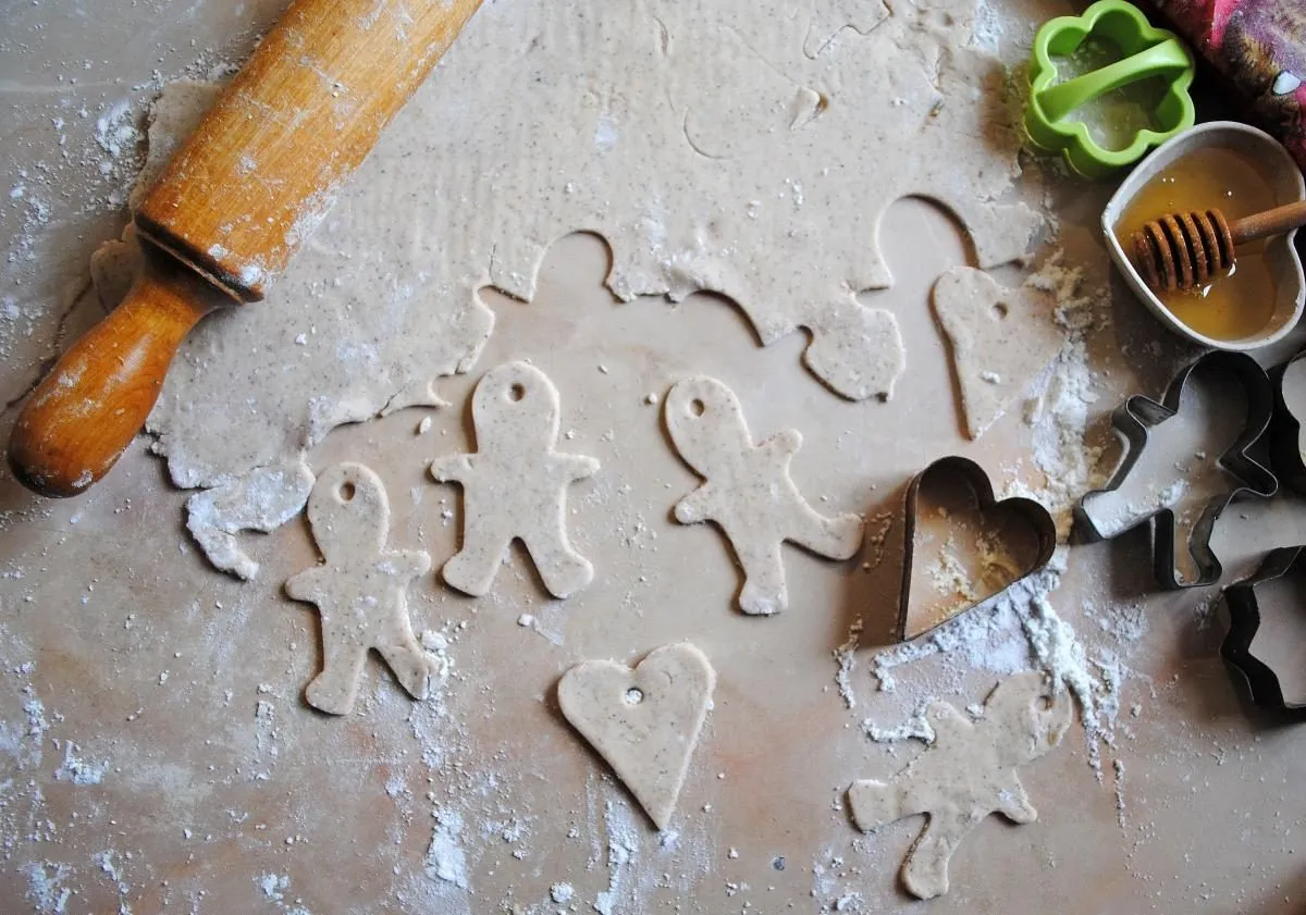 Przygotowania do pieczenia piernik&oacute;w bezglutenowych. Ciasto, wałek, foremki w kształcie ludzik&oacute;w i serc, mi&oacute;d.