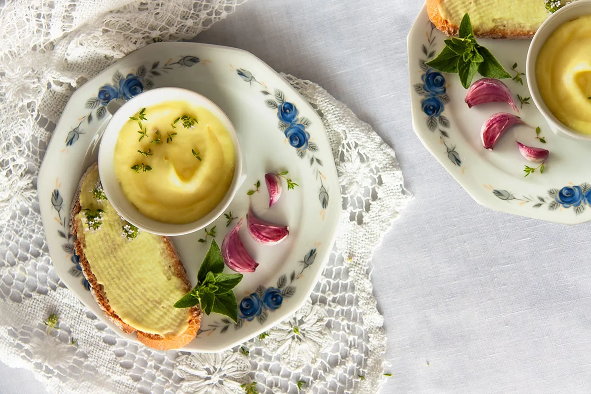 Jak zrobić masło roślinne? Kremowa pasta na chlebie, czosnek i zioła na talerzu.