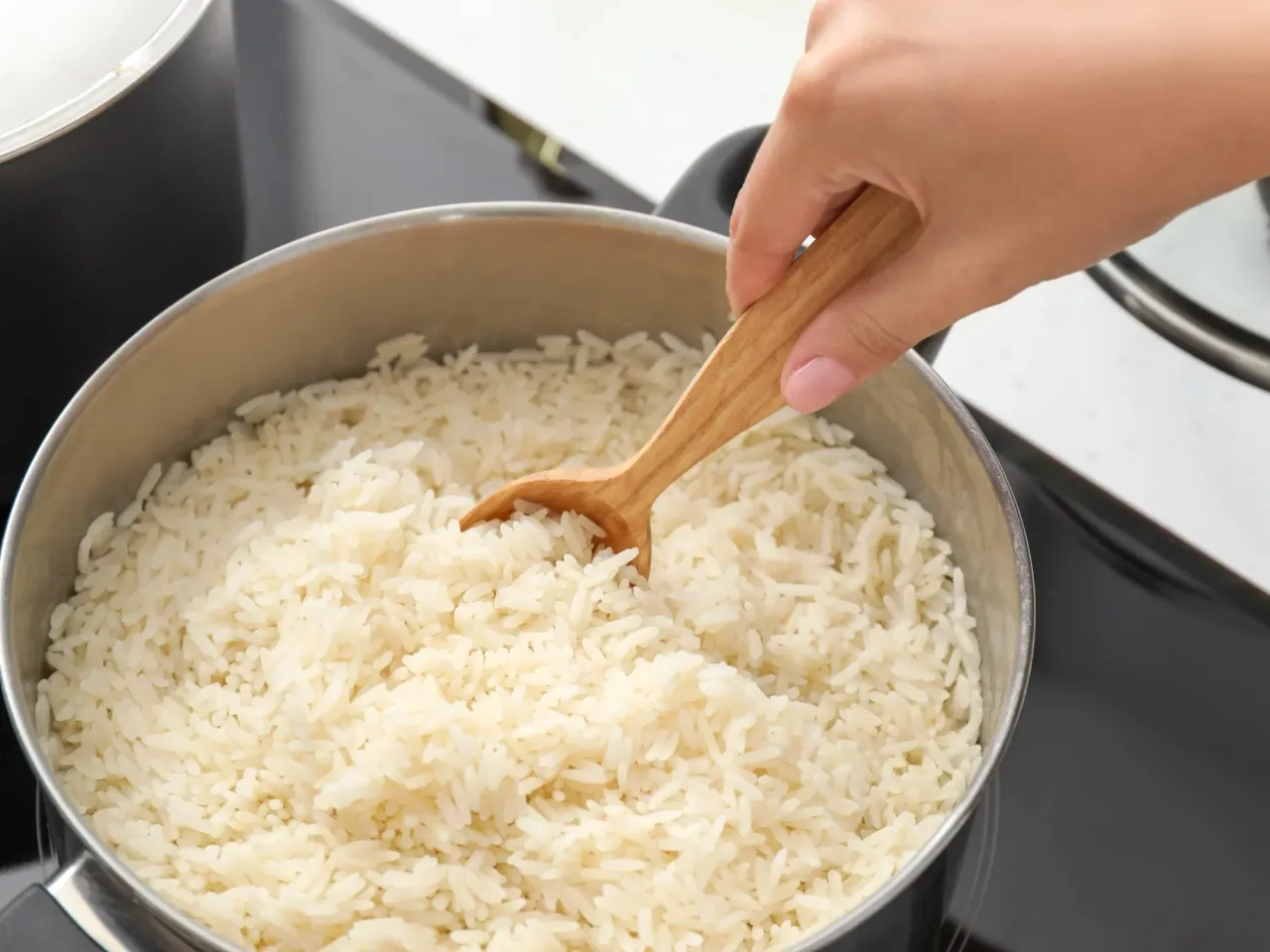 Drobny, puszysty ryż basmati gotuje się w garnku. Drewniana łyżka miesza go, pokazując, jak ugotować ryż basmati.