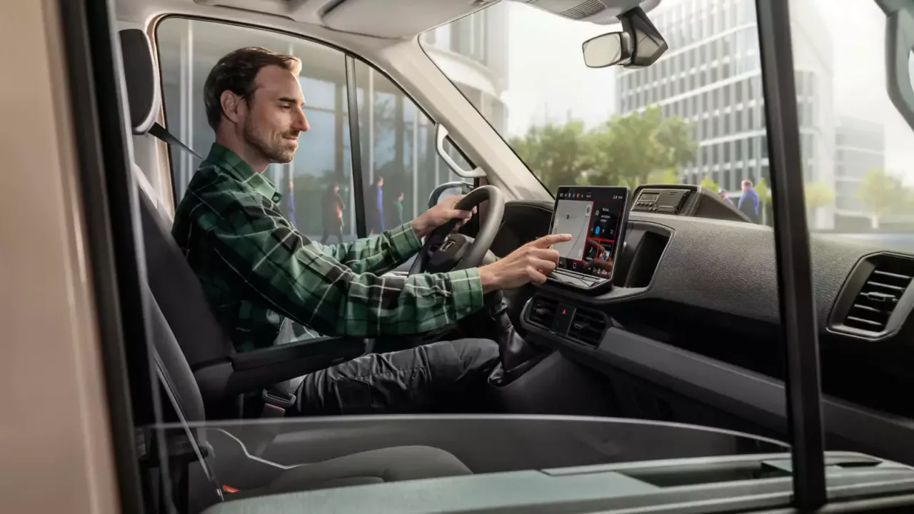 Mężczyzna w zielonej koszuli sprawdza na ekranie, ile pali bus. Nowoczesny kokpit z nawigacją.