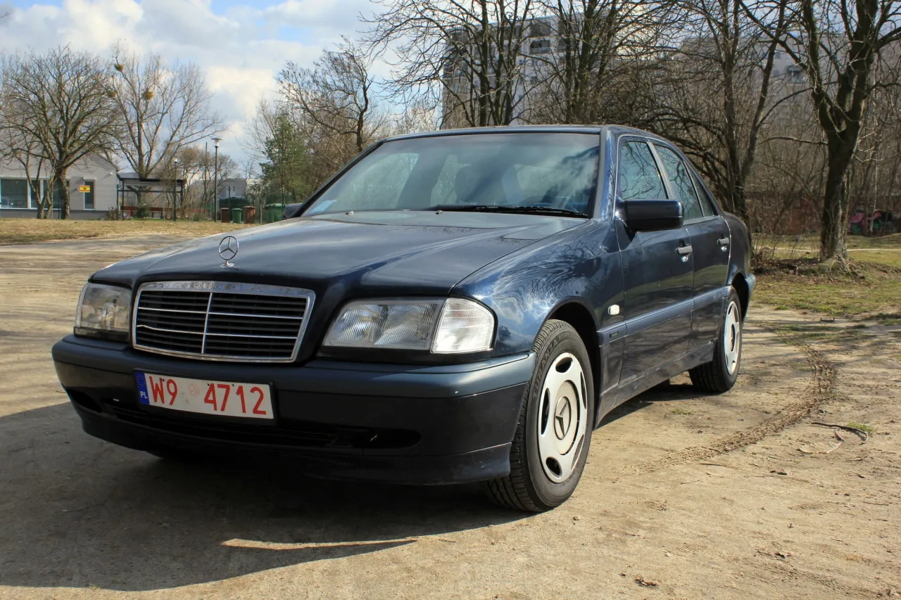 Ciemnoniebieski Mercedes-Benz C-klasa W202 na tle drzew i budynków.