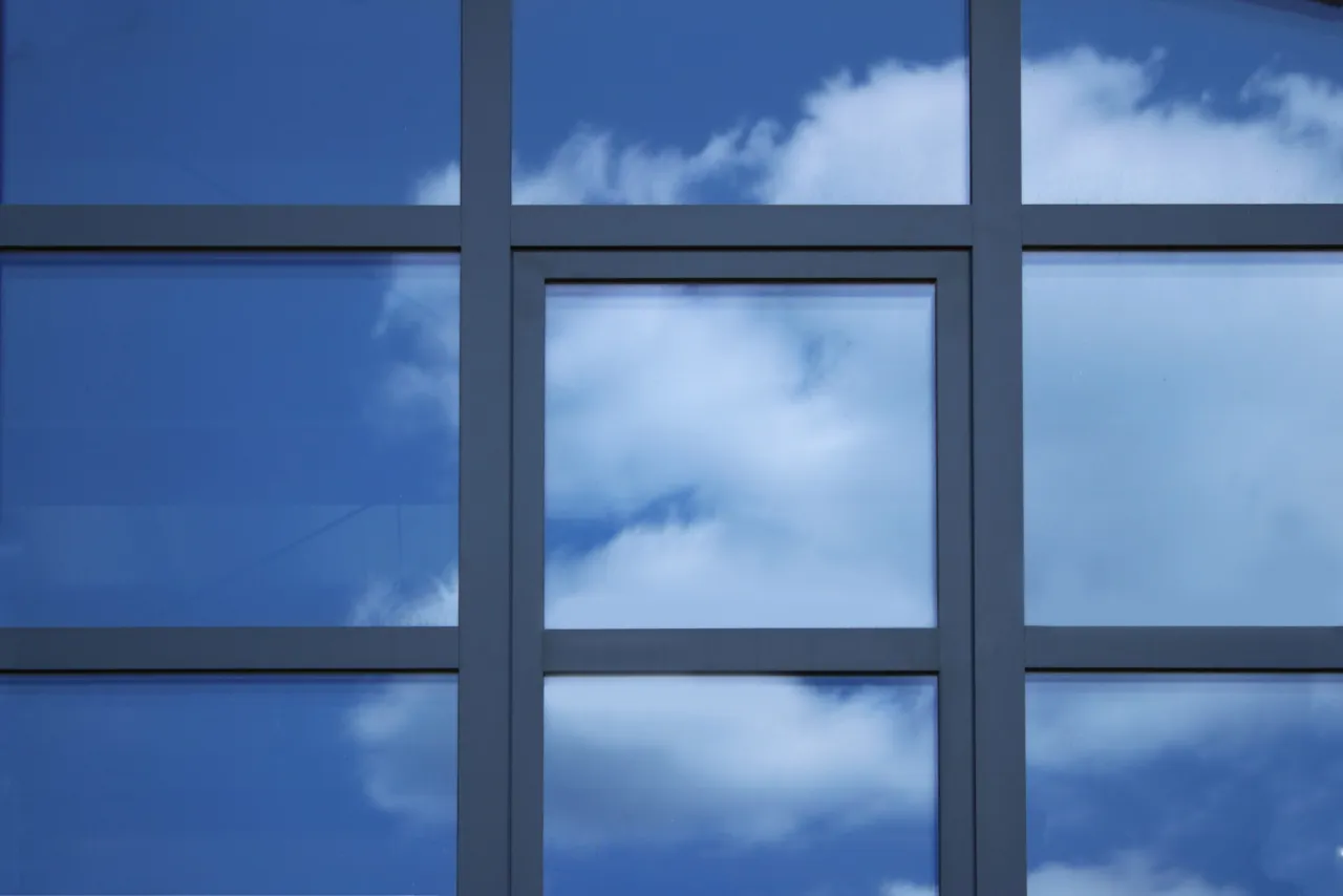 Szkło odbija błękitne niebo z chmurami. Eleganckie szprosy do okien tworzą geometryczny wzór, dzieląc przestrzeń na kwadraty.