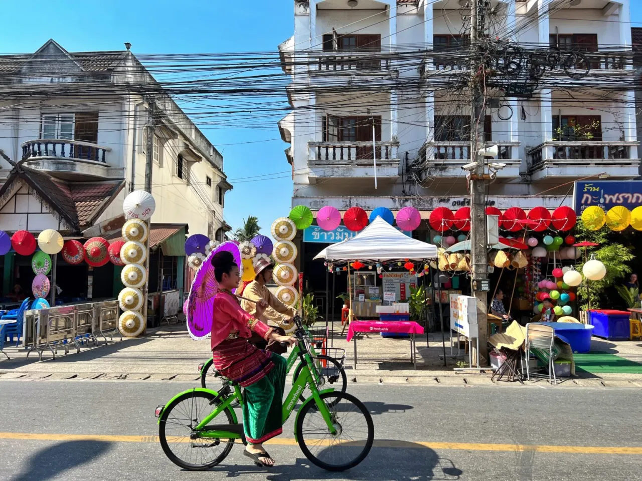 Kolorowe parasolki i tradycyjne stroje w Chiang Mai, gdzie nocować? Rowerzyści w barwnych strojach przemierzają ulicę pełną lokalnych wyrobów.
