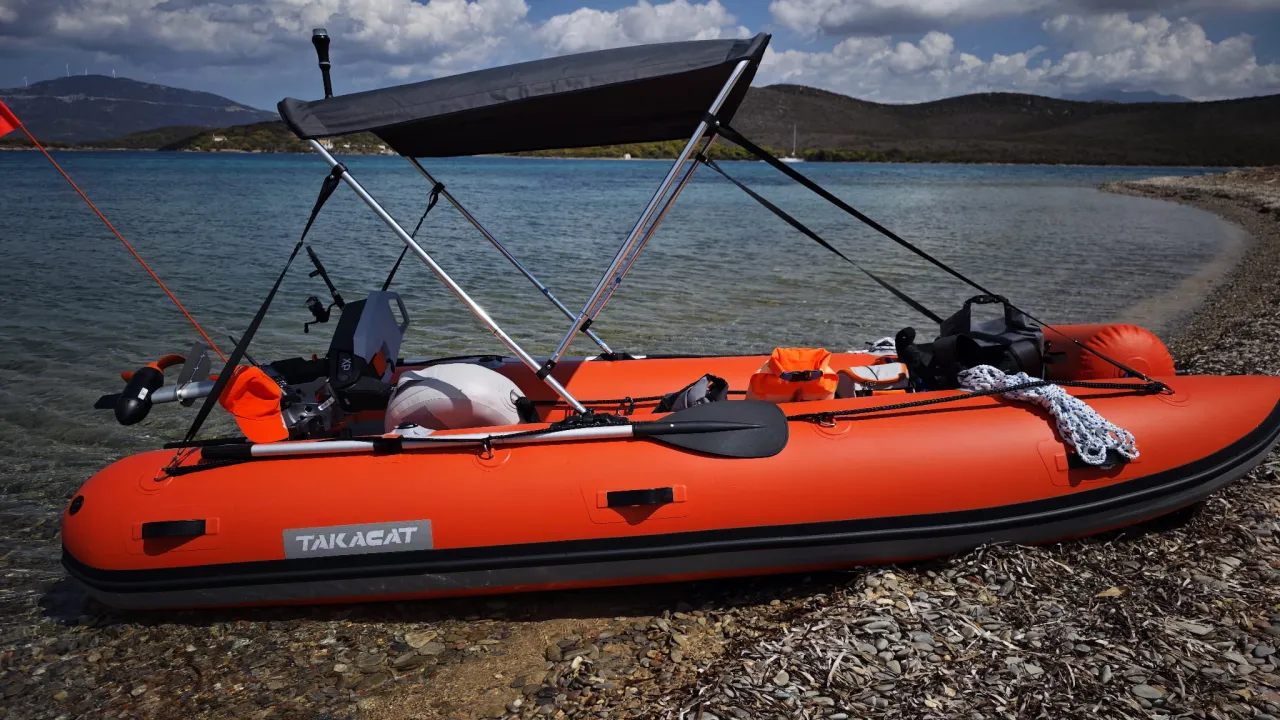 Pomarańczowy ponton TAKACAT, idealny na ryby, z silnikiem elektrycznym, wiosłem i kamizelkami ratunkowymi, gotowy do wodowania.