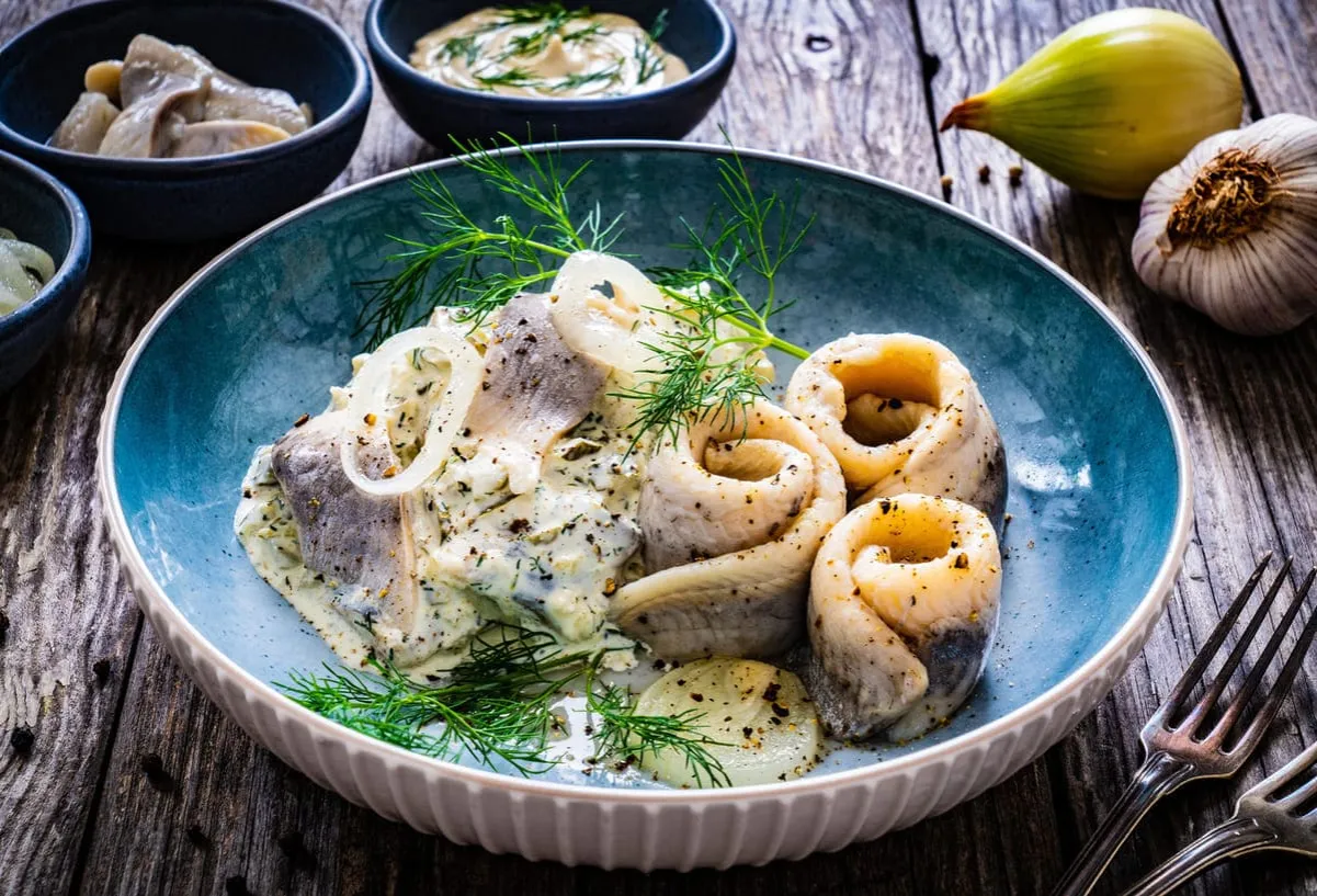 Jak zrobić sałatkę śledziową? Śledzie w sosie śmietanowym z cebulą i koperkiem, podane na drewnianym stole.