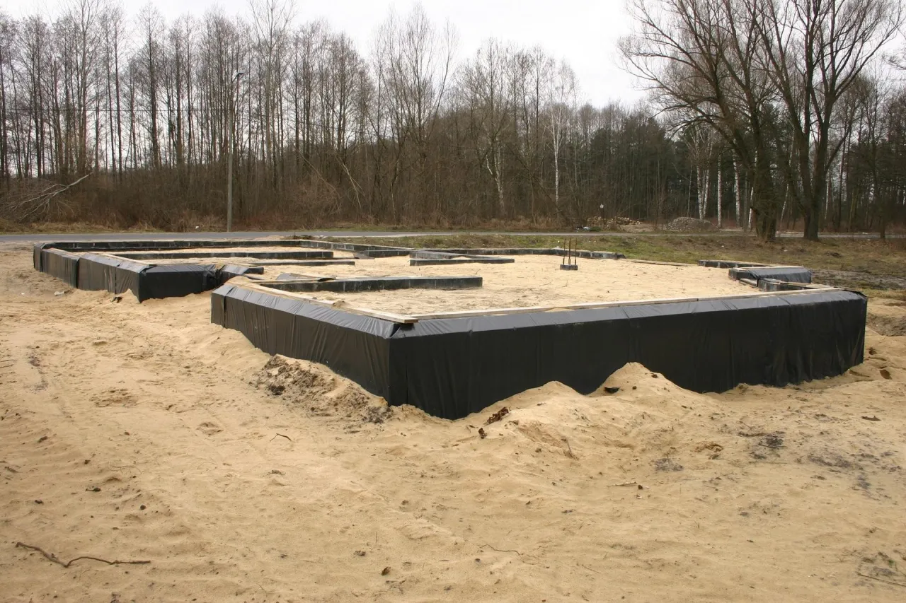 Fundament domu w piasku, otoczony czarną folią jako środek do izolacji fundament&oacute;w.