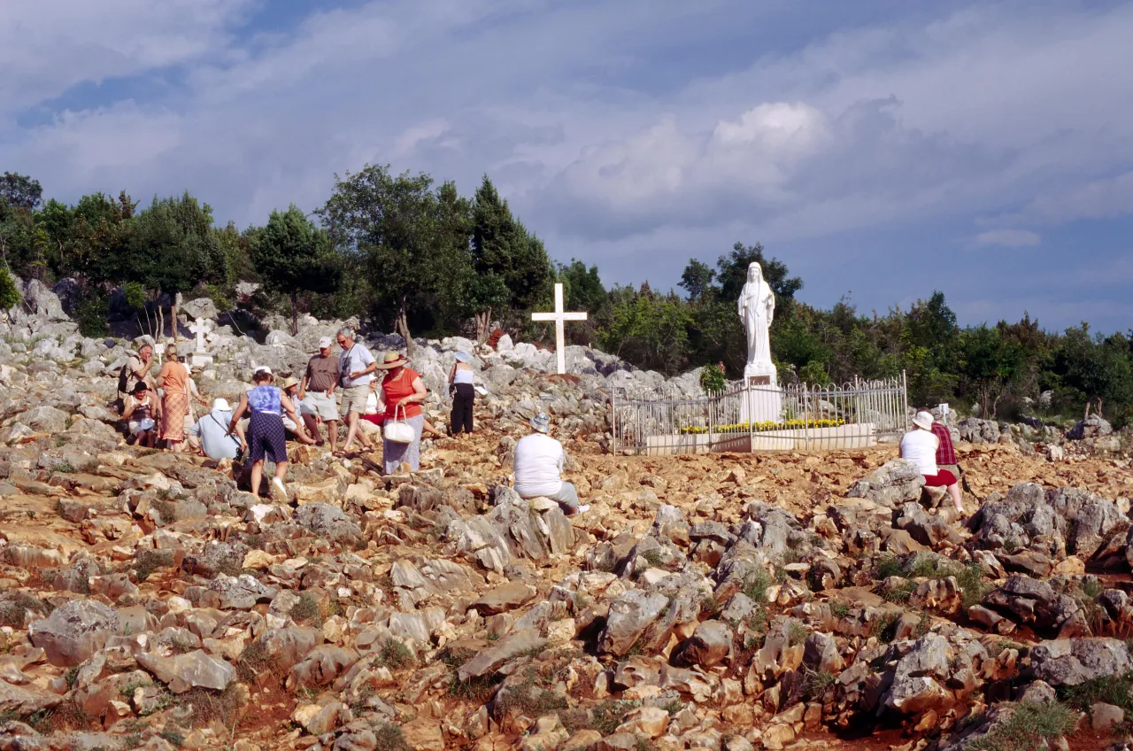 Pielgrzymi na skalistym wzg&oacute;rzu w Medziugorie, obok figury Matki Bożej i krzyża. Czy w Medziugorie jest bezpiecznie? Tak, miejsce to przyciąga wielu wiernych.