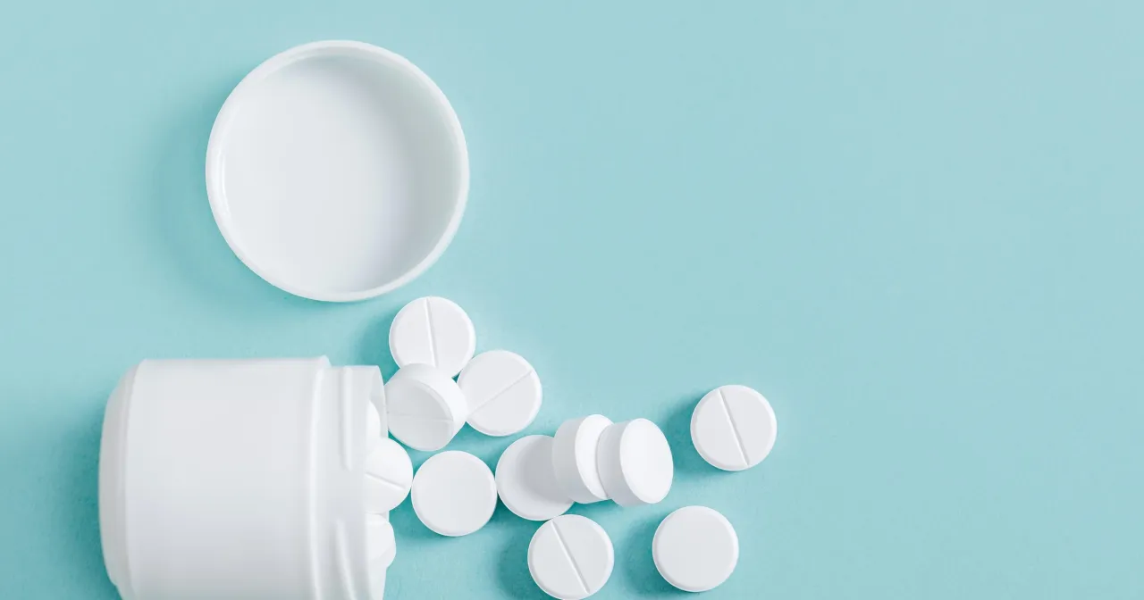 Białe tabletki rozsypane obok otwartego pojemnika. Czy Controloc jest bezpieczny? Pytanie o bezpieczeństwo leku.