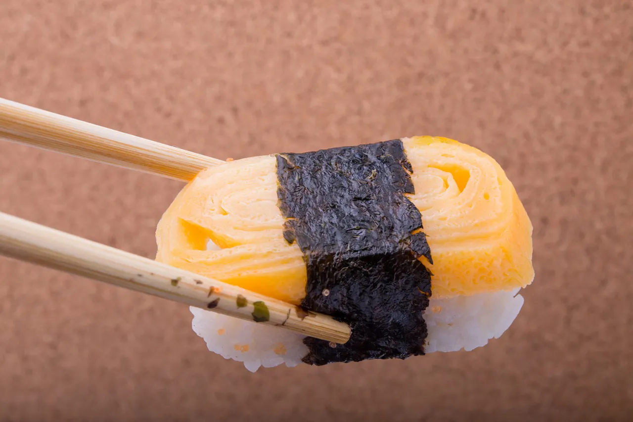 Sushi z tamago, ryżem i nori, trzymane pałeczkami. Idealny przepis na tamago do sushi.