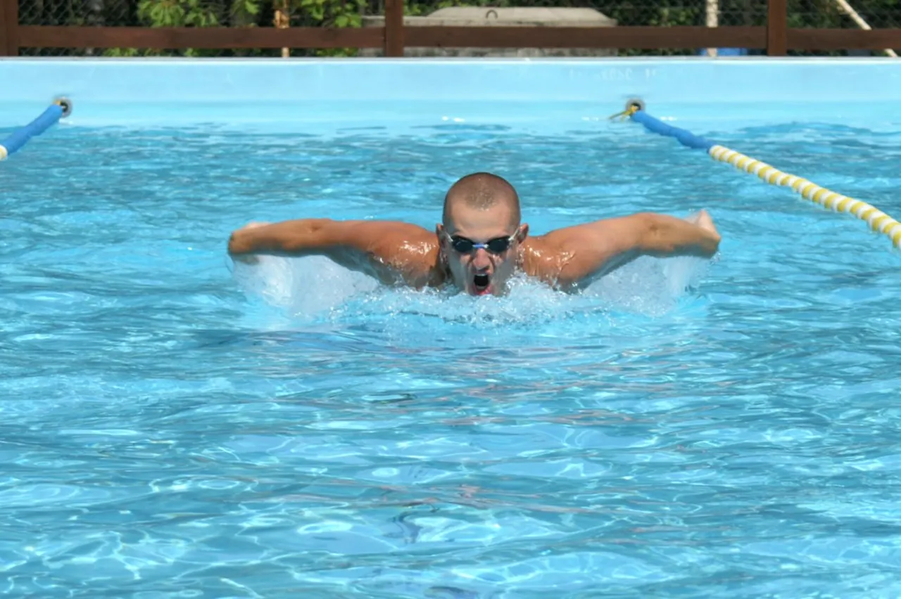 Pływak wykonuje styl motylkowy, jeden z najtrudniejszych styl&oacute;w pływania. Woda rozpryskuje się wok&oacute;ł jego ramion.