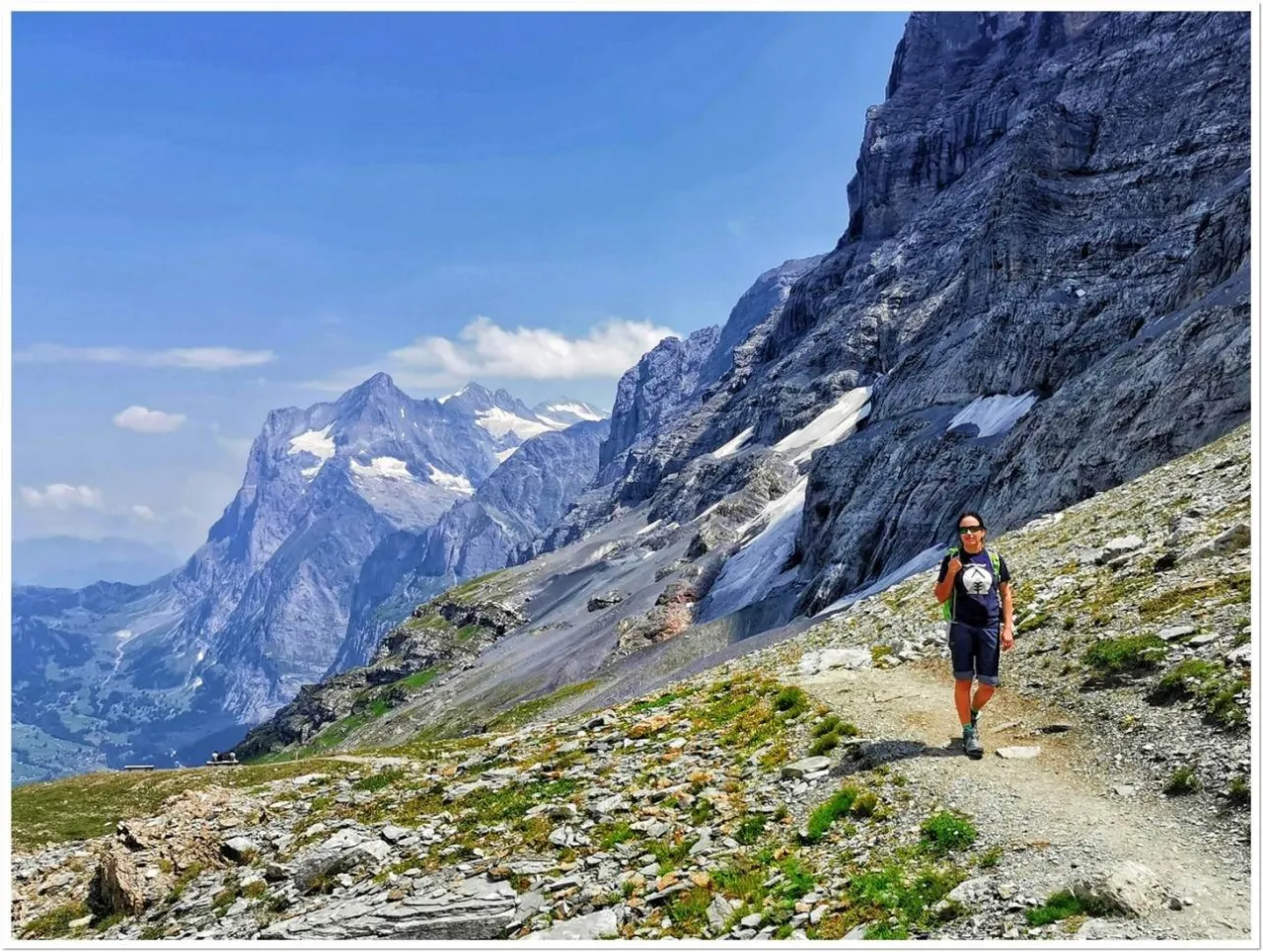 Szwajcaria latem: turystka wędruje szlakiem pośr&oacute;d skalistych g&oacute;r i zielonych zboczy, podziwiając majestatyczne alpejskie krajobrazy.