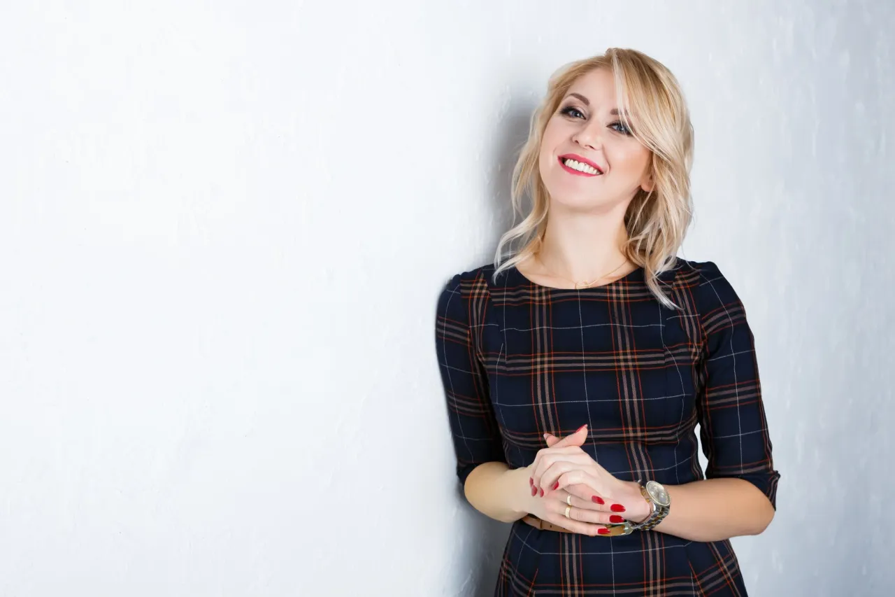 Uśmiechnięta blondynka w kratkowej sukience. Idealny przykład, jak zrobić zdjęcie do CV telefonem &ndash; profesjonalnie i z klasą.