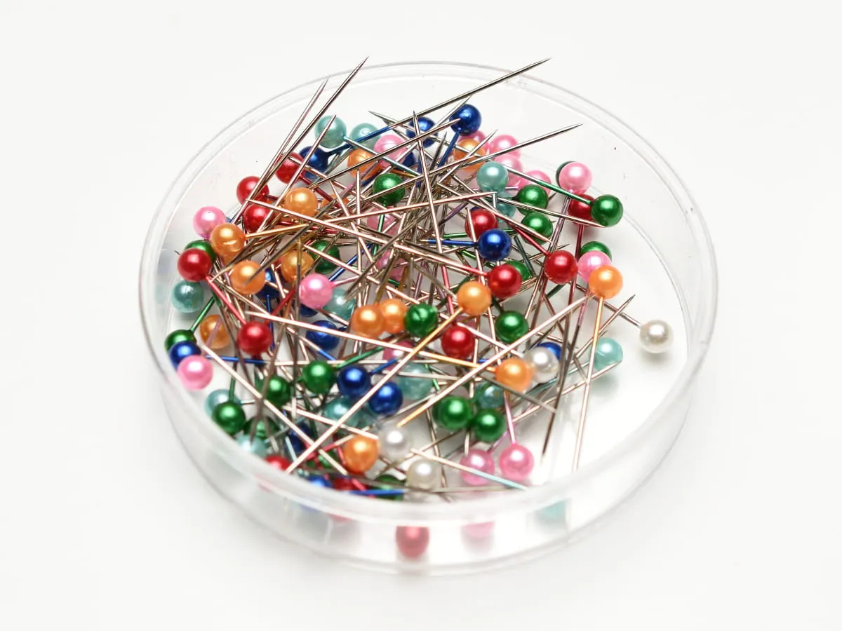 Kolorowa gł&oacute;wka szpilki w przezroczystym pojemniku. Wiele igieł z kolorowymi, perłowymi gł&oacute;wkami.