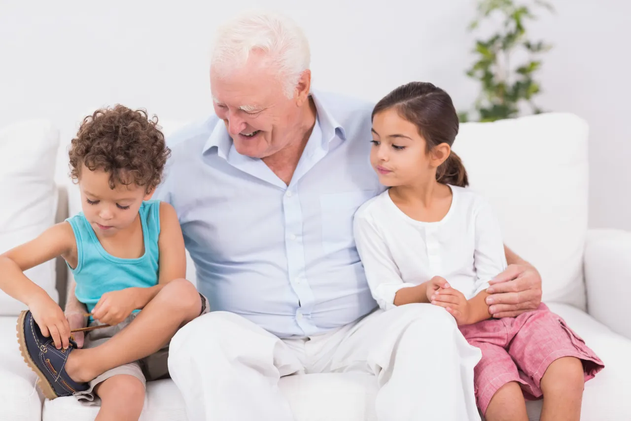 Dziadek uczy wnuka, jak nauczyć dziecko wiązać buty. Wnuczka patrzy z zaciekawieniem.