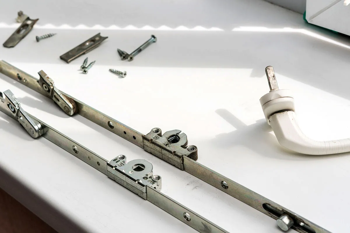 Części okucia okiennego i klamka leżą na parapecie, gotowe do montażu, by jak zamknąć okno.