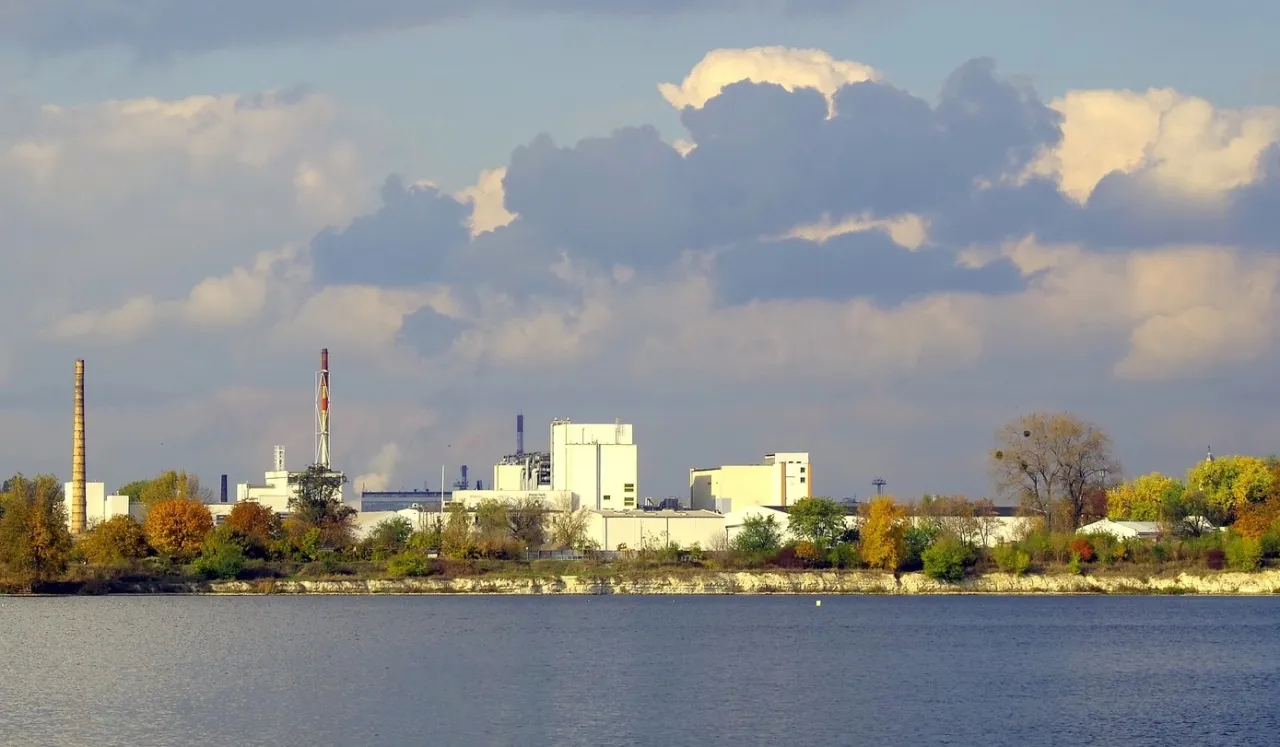 Przemysłowe budynki i kominy nad rzeką. Takie obiekty często są gł&oacute;wnymi źr&oacute;dłami zanieczyszczeń wody.