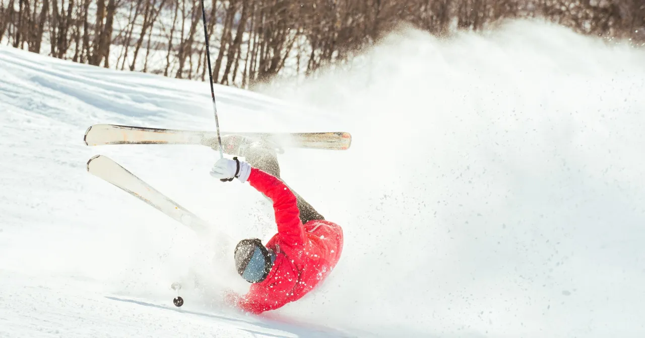 Narciarz w czerwonej kurtce doświadcza nieoczekiwanego wypadku na nartach, wzbijając chmurę śniegu.