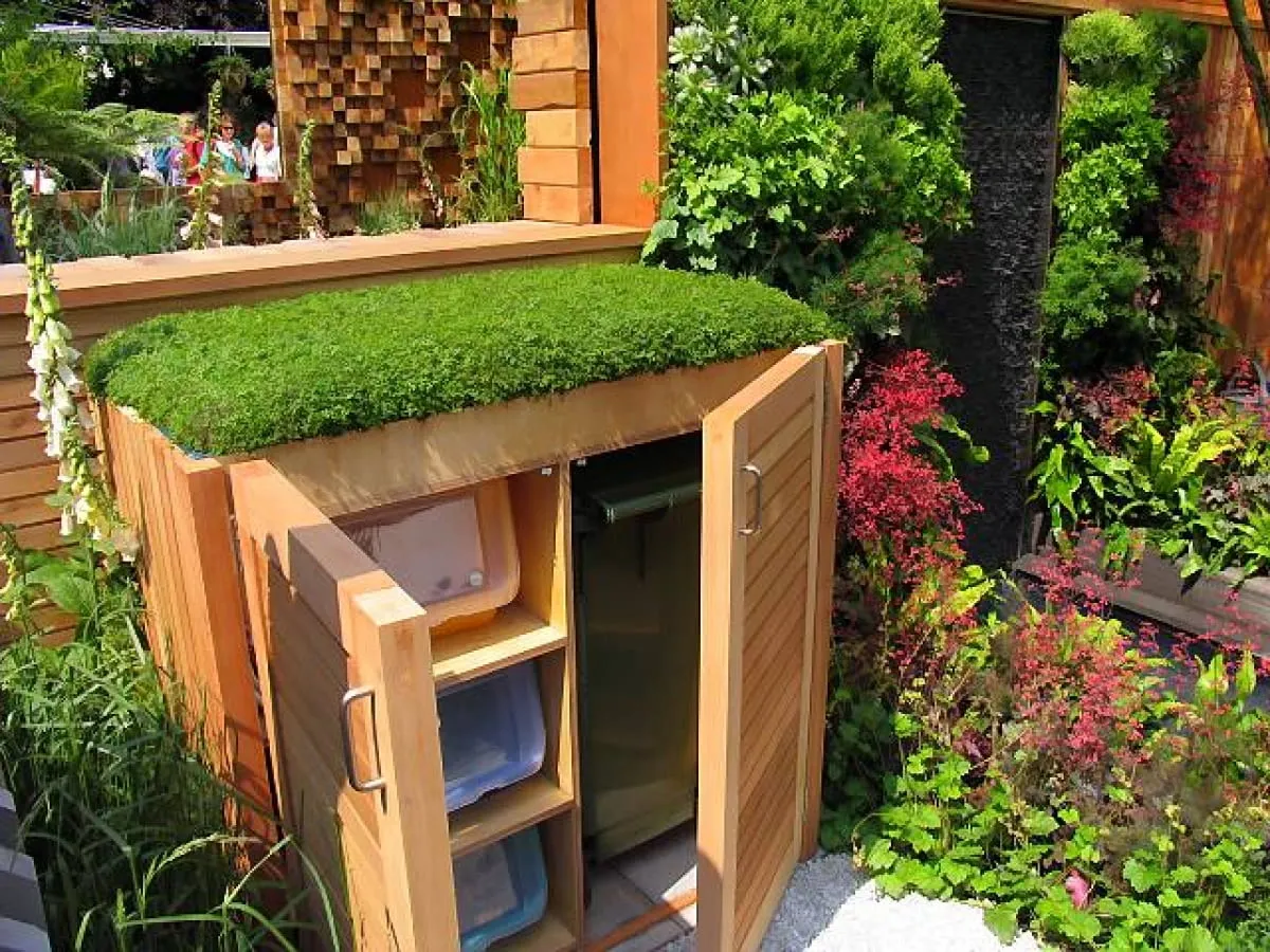 Pomysł, jak ukryć kosz na śmieci w ogrodzie: drewniana skrzynia z zielonym dachem, idealnie wkomponowana w roślinność.