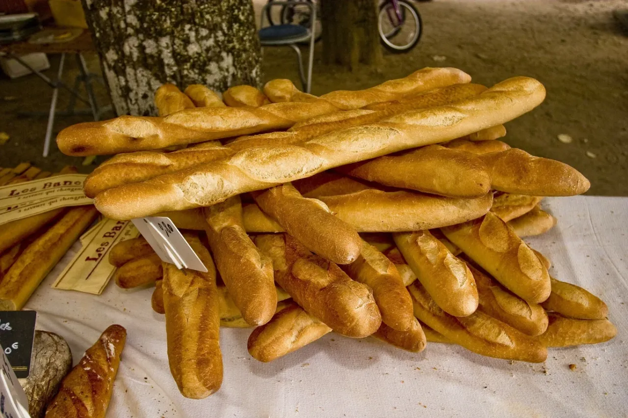 Stos świeżych bagietek, charakterystyczne potrawy kuchni francuskiej, na stole przykrytym białym obrusem.