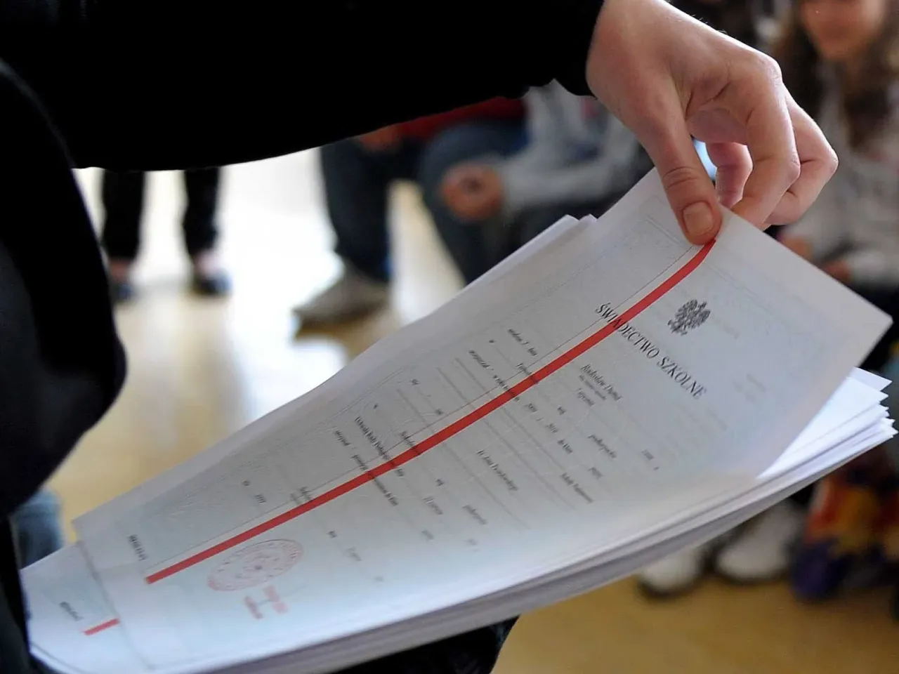 Dłoń trzyma stos świadectw szkolnych. Czy religia liczy się do średniej? To pytanie nurtuje wielu uczniów, gdy patrzą na swoje oceny.