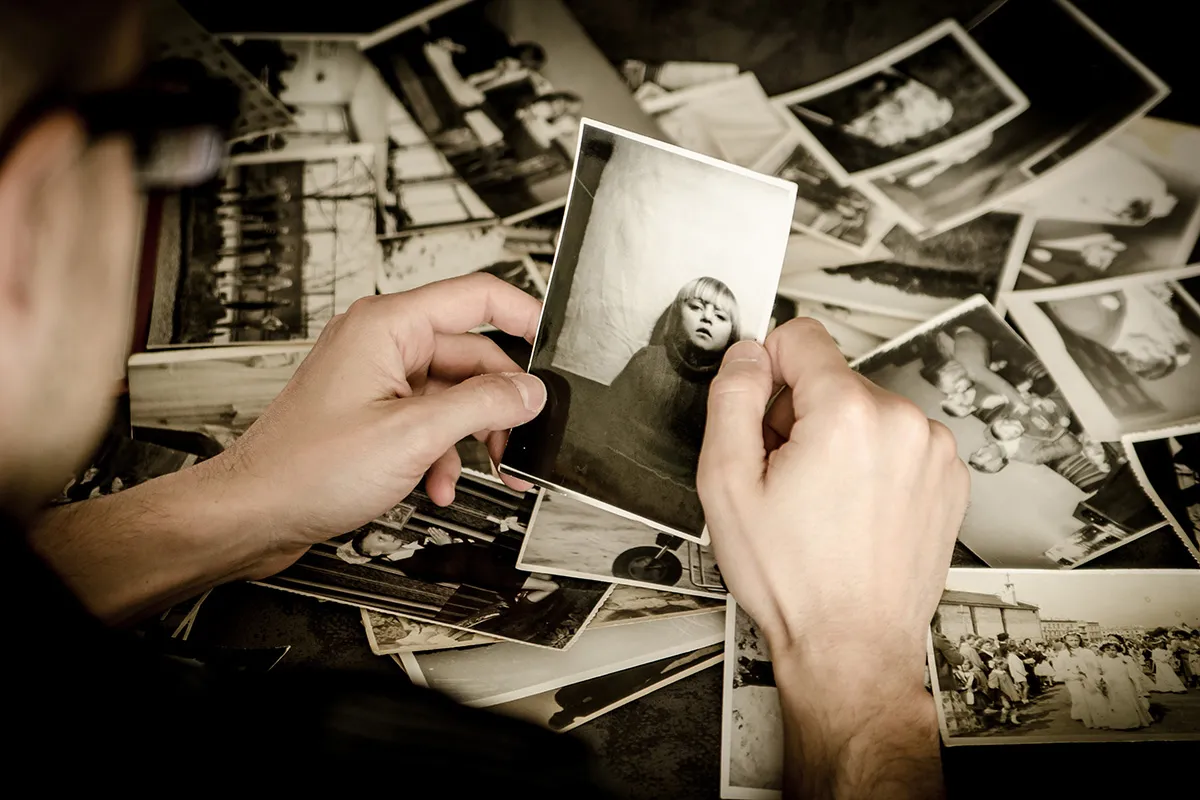 Dłonie przeglądają stos starych fotografii. Czy fotograf przechowuje zdjęcia, by wr&oacute;cić do wspomnień?