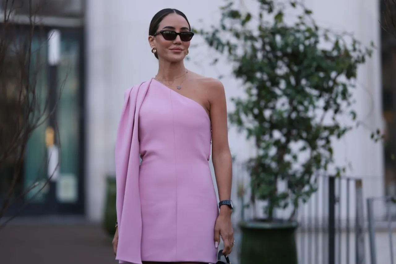 Elegancka fryzura do sukienki na jedno ramię w kolorze pudrowego r&oacute;żu. Kobieta w okularach przeciwsłonecznych i złotej biżuterii.