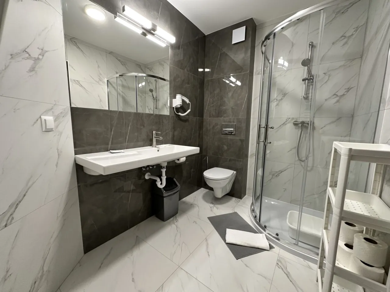 Nowoczesna łazienka z prysznicem, umywalką i toaletą. Idealna, by poczuć się komfortowo, gdy zastanawiasz się, jaki wybrać pokój w sanatorium.