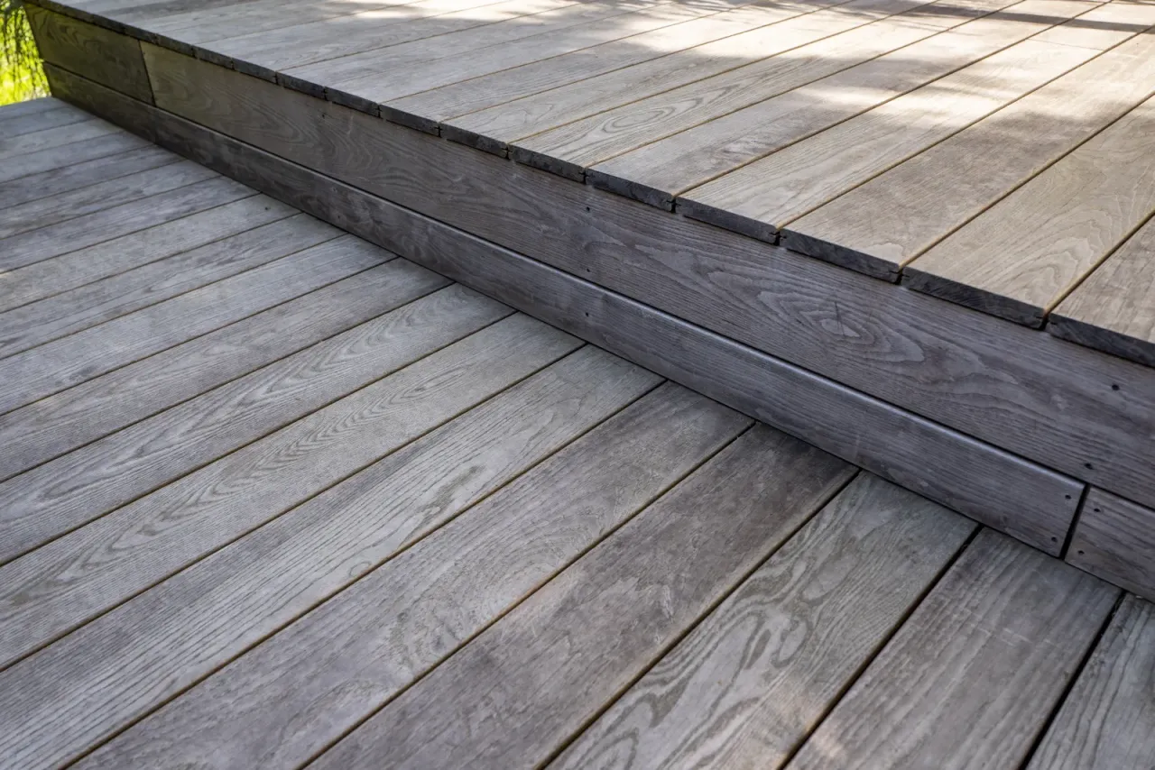Szare, drewniane deski tarasowe, idealne jako materiał na meble ogrodowe. Wyglądają na trwałe i odporne na warunki atmosferyczne.