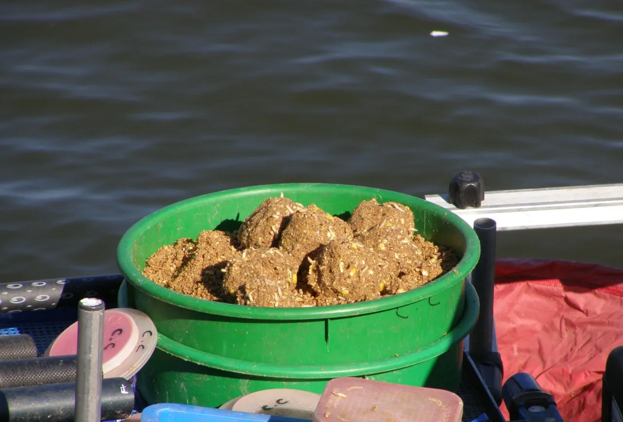 Zielone wiadro z kulami zanęty, kt&oacute;ra może być najlepsza zanęta na leszcze. W tle woda.