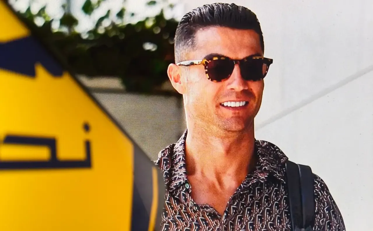 Cristiano Ronaldo w okularach przeciwsłonecznych i wzorzystej koszuli, uśmiecha się. Jego wysokie cristiano ronaldo zarobki pozwalają na taki styl życia.