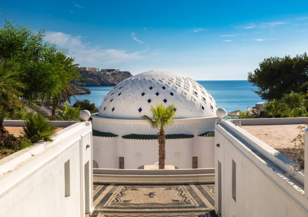 Biała kopuła z niebieskimi rombami, otoczona palmami i mozaikową posadzką, nad błękitnym morzem. To jedno z najpiękniejszych miejsc na Rodos.