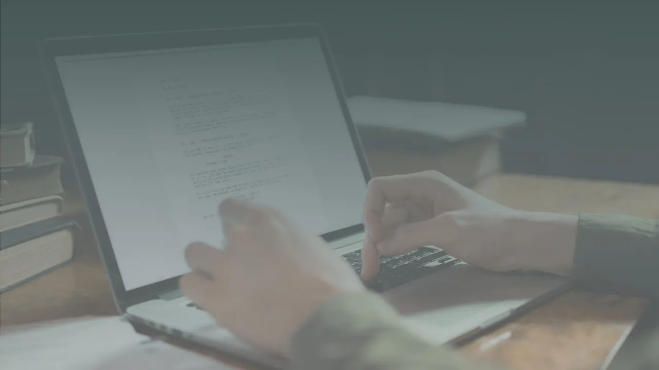 Ręce piszą scenariusz na laptopie, pokazując, jak napisać książkę. Obok stos książek.