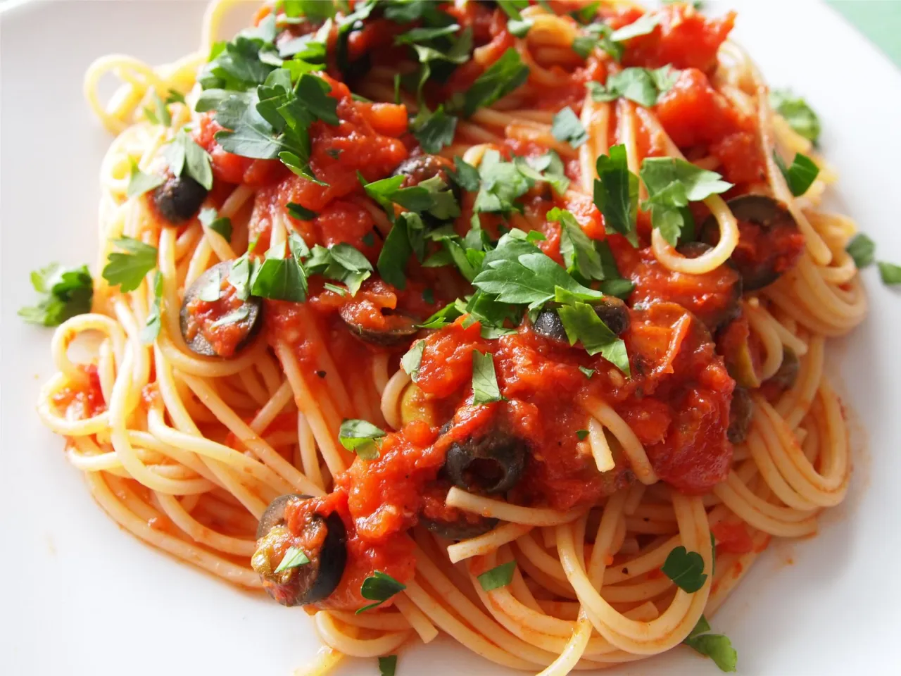 Pyszne Spaghetti Puttanesca przepis: makaron z sosem pomidorowym, czarnymi oliwkami i natką pietruszki.