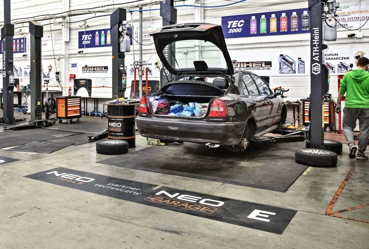 Warsztat samoobsługowy Warszawa: samochód na podnośniku, bagażnik otwarty, narzędzia i części widoczne.