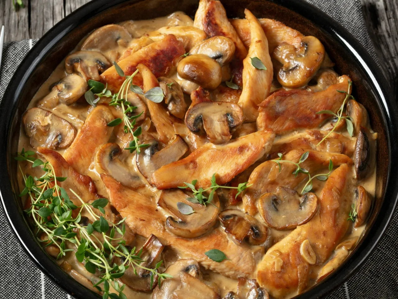 Polędwiczki drobiowe w sosie grzybowym, udekorowane świeżym tymiankiem. Pyszne danie gotowe do podania.