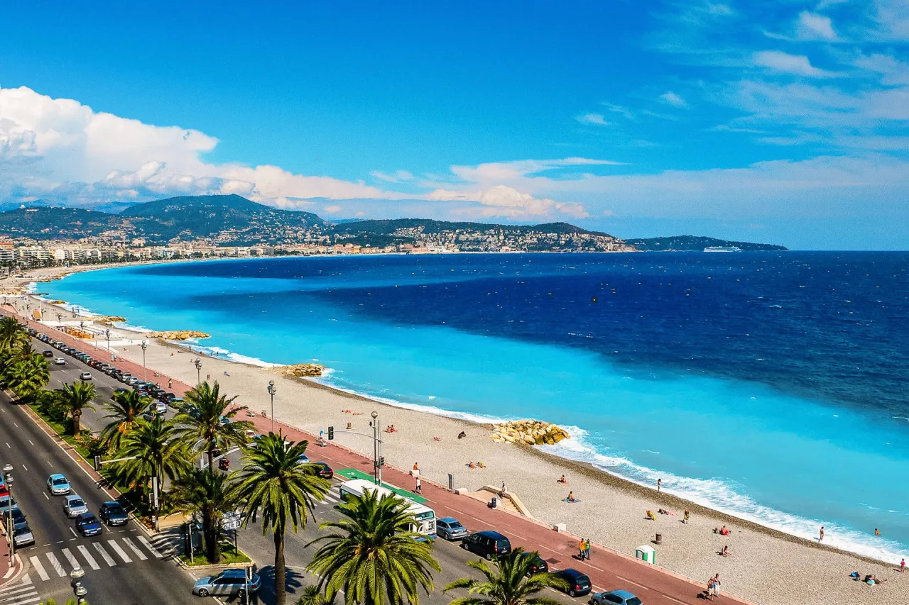 Widok na Lazurowe Wybrzeże Francji z palmami, plażą i turkusowym morzem.