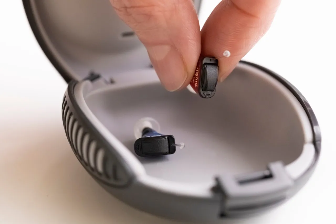 Dłoń wkłada aparat słuchowy do etui. Dowiedz się, jak wyregulować aparat słuchowy, aby cieszyć się lepszym dźwiękiem.