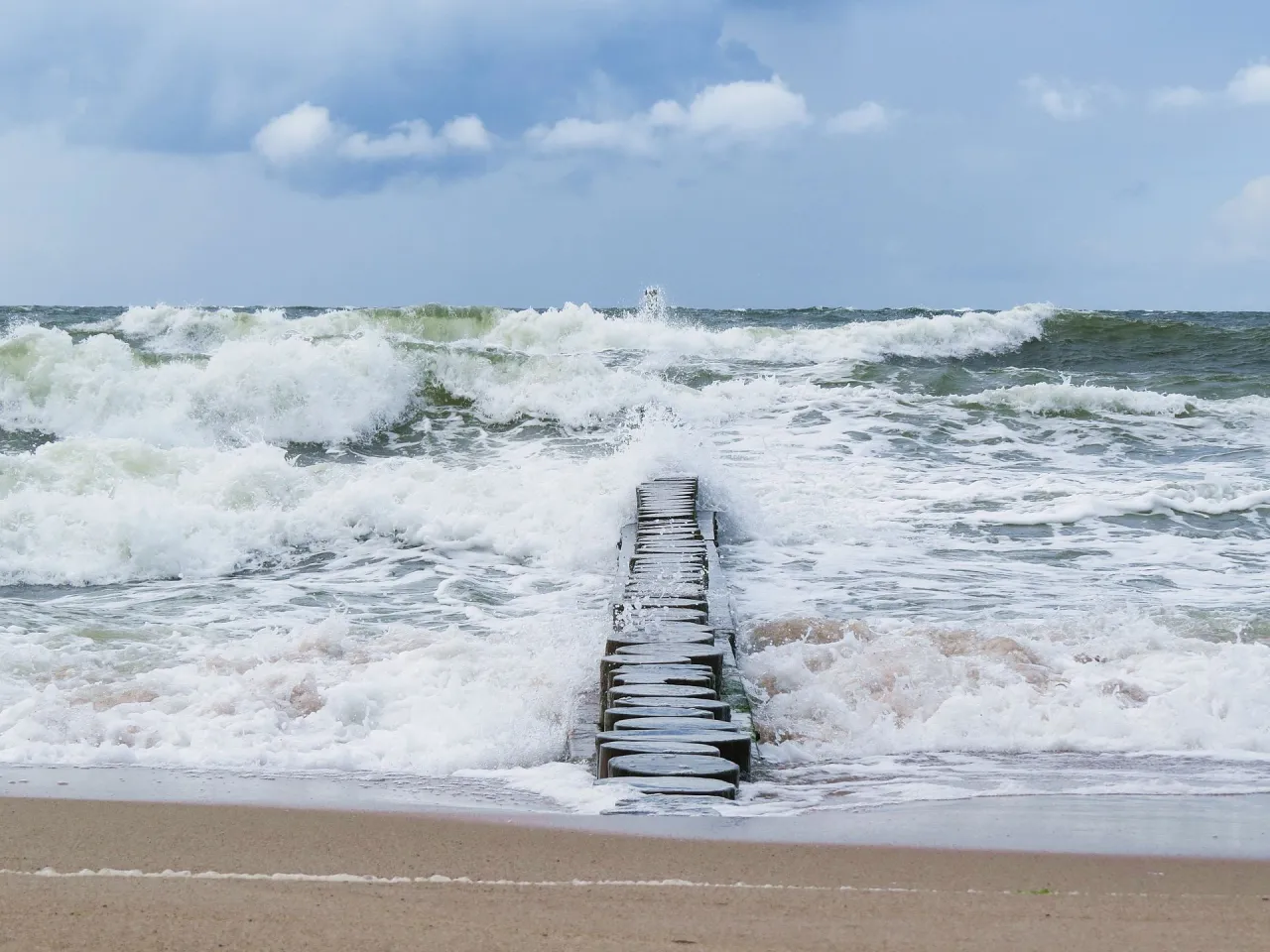 Drewniany falochron walczy z potężnymi falami, kiedy sztorm na Bałtyku szaleje. Woda pieni się i rozbija o brzeg.