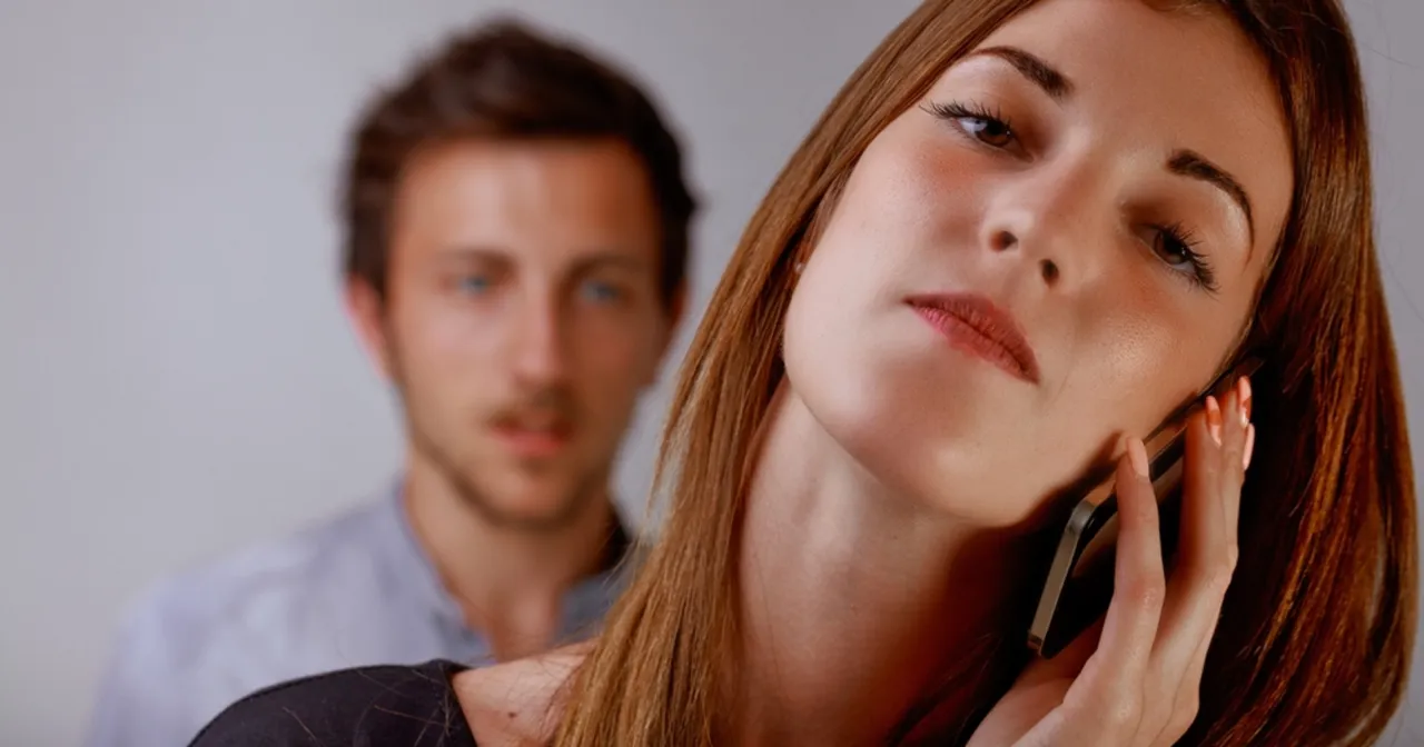 Kobieta rozmawia przez telefon, podczas gdy mężczyzna z tyłu patrzy z niepokojem. Jak rozmawiać z narcyzem?