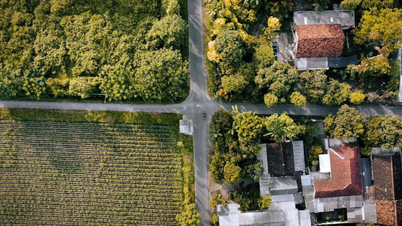 Widok z lotu ptaka na skrzyżowanie dr&oacute;g, pola uprawne i domy. To może być działka inwestycyjna, co to znaczy? Potencjał rozwoju.