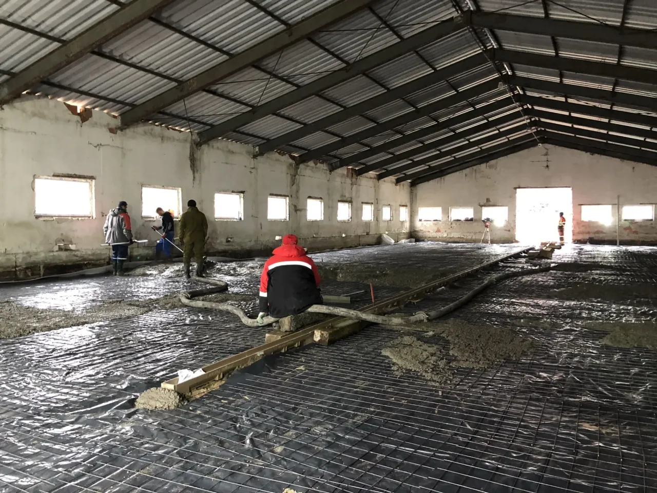 Pracownicy przygotowują podłoże pod wylewkę betonową, układając folię i zbrojenie w hali.