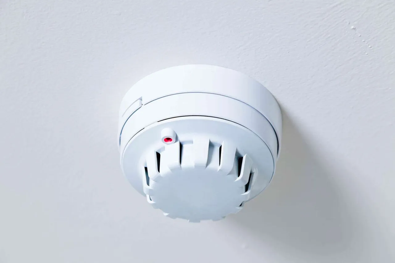 Biały czujnik czadu na suficie, z czerwoną diodą. Pokazuje, jak działa czujnik czadu, monitorując powietrze.