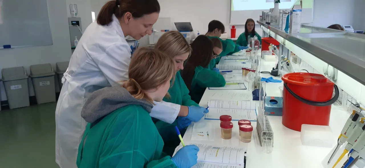 Nauczycielka w białym fartuchu pokazuje uczniom, kto pracuje w laboratorium medycznym, podczas zajęć praktycznych.
